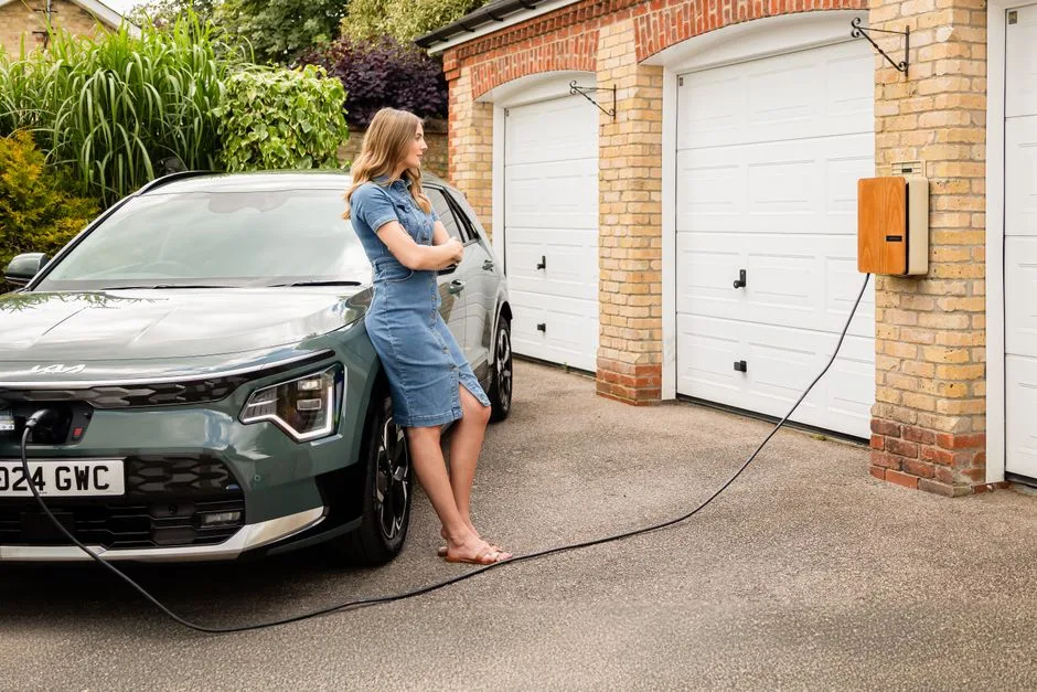 Femme chargeant son véhicule électrique à domicile sur une borne murale, contexte d'une maison individuelle